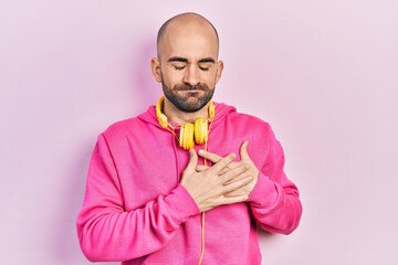 Young bald man wearing gym clothes and using headphones smiling with hands on chest with closed eyes and grateful gesture on face. health concept.