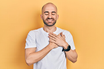 Young bald man wearing casual white t shirt smiling with hands on chest with closed eyes and grateful gesture on face. health concept.