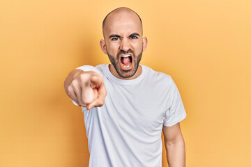 Young bald man wearing casual white t shirt pointing displeased and frustrated to the camera, angry...