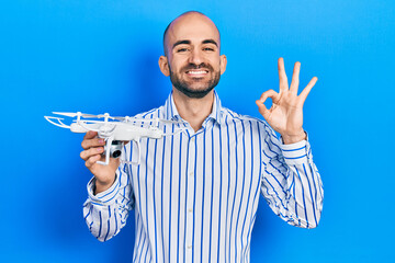 Naklejka premium Young bald man holding drone doing ok sign with fingers, smiling friendly gesturing excellent symbol