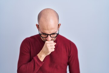Young bald man with beard standing over white background wearing glasses feeling unwell and...