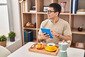 Young man having breakfast using touchpad at home