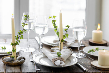 Rustic zero waste wedding decor with natural elements. Wooden table, candles, linen napkins, branches with green leaves. Eco-friendly decoration for the special dinner. Romantic and cozy place
