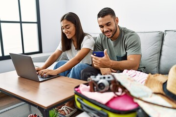Latin man and woman couple smiling confident paying for travel using laptop and credit card at home