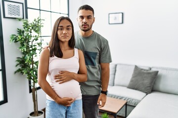 Young interracial couple expecting a baby, touching pregnant belly relaxed with serious expression...