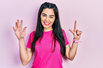 Young hispanic girl wearing casual pink t shirt showing and pointing up with fingers number seven while smiling confident and happy.