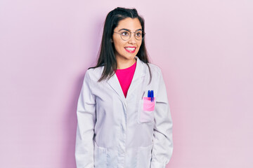 Young hispanic girl wearing scientist uniform looking away to side with smile on face, natural...