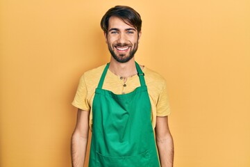 Young hispanic man wearing cleaner apron and gloves with a happy and cool smile on face. lucky...