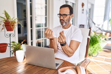 Middle age man using computer laptop at home doing money gesture with hands, asking for salary...