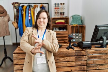 Young down syndrome woman working as manager at retail boutique disgusted expression, displeased and fearful doing disgust face because aversion reaction. with hands raised
