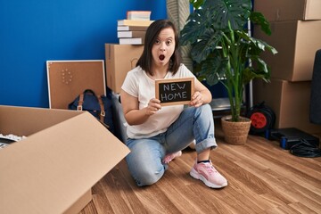 Hispanic girl with down syndrome sitting on the floor at new home afraid and shocked with surprise and amazed expression, fear and excited face.