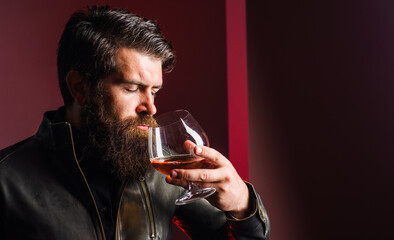 Brutal man tasting whiskey. Strong alcohol. Bearded guy in leather jacket sniffing brandy or cognac.