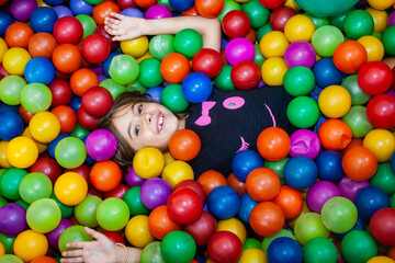 young happy girl covered in colorful plastic balls in a ball pit