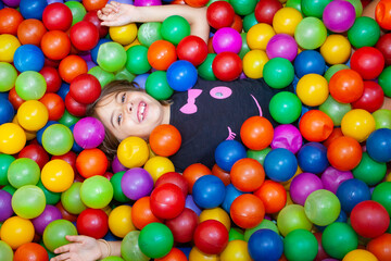 Fototapeta na wymiar young happy girl covered in colorful plastic balls in a ball pit