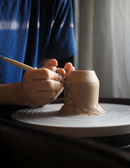 Ceramist at work using tools for creating handmade vase in studio, selective focus. Close up of female potter hands sharing handcraft crockery in studio. Small business, art, hobby concept.