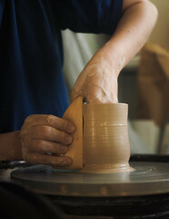 Fototapeta na wymiar Young female master working on a potter’s wheel, creates clay dishes. Ceramist young woman making clay product on pottery lathe in studio, workshop, side view. Small business, hobby, ceramic concept.