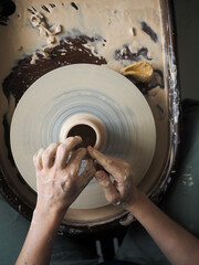 Young female master working on a potter’s wheel, creates clay dishes. Ceramist young woman making...