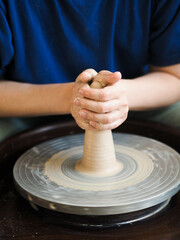 Young female master working on a potter’s wheel, creates clay dishes. Ceramist young woman making clay product on pottery lathe in her studio, workshop, front view.