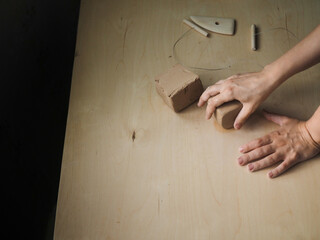 Young woman preparing clay to create a mug on a wooden table. Ceramist young woman preparing clay to make pottery pieces in her studio; anonymous hands at work. Small business, hobby, ceramic concept.