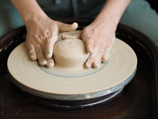 Young female master working on a potter’s wheel, creates clay dishes. Ceramist young woman making clay product on pottery lathe in her studio, workshop top view.