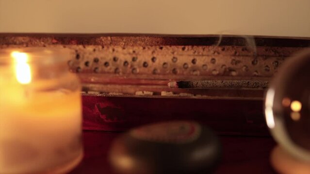 Incense stick burning inside wood incense burner with black stone, white candle