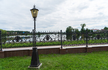 Broken old vintage street lamp or lantern near a carved forged fence on the shore of a pond, Nevyansk, Russia on a summer day