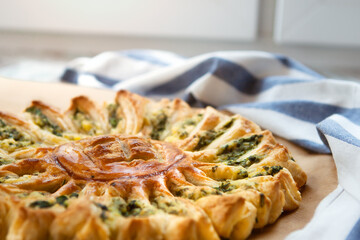 Delicious pie with spinach and ricotta cheese in the shape of a sunflower, towel next to it, close-up.