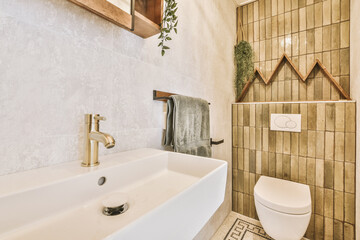 Modern flush toilet and ceramic sink installed on white tiled walls near mirror and towel in small...