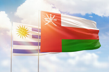 Sunny blue sky and flags of oman and uruguay