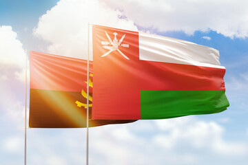 Sunny blue sky and flags of oman and angola
