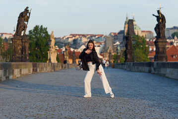 Young woman in casual stylish clothes dancing on the stone bridge of old town in a Prague. Active...