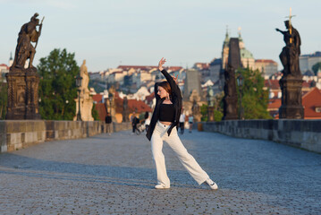 Young woman in casual stylish clothes dancing on the stone bridge of old town in a Prague. Active...
