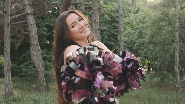 Portrait of beautiful cheerleader woman dancing with pompons outdoors in the park on sunset
