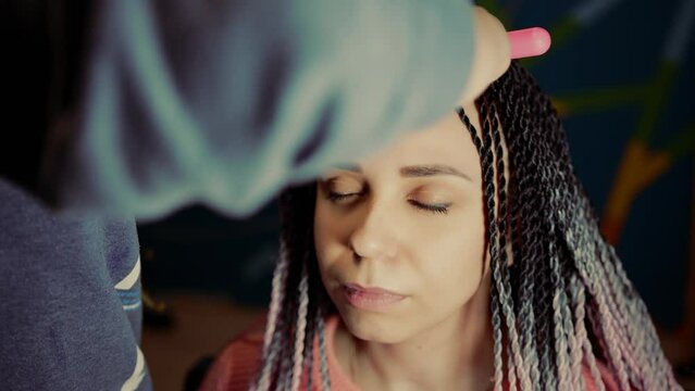 A female stylist attaches Senegalese braids to a woman in a beauty salon. Portrait of a beautiful lady with Senegalese pigtails in casual clothes. A hipster girl gets her hair done