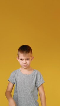 Disappointed child. Dislike gesture. Bad idea. Refusal signal. Vertical portrait of dissatisfied skeptic boy showing thumb down stop nope disapproval sign isolated on yellow copy space background.