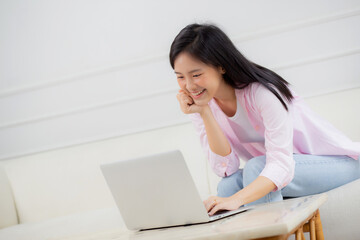 Young asian business woman work from home with laptop computer online to internet on sofa in living room, freelance girl using notebook sitting on couch with comfort and relax, lifestyles concept.