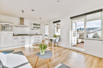 Interior of light kitchen and dining room with balcony doors in contemporary apartment at daytime