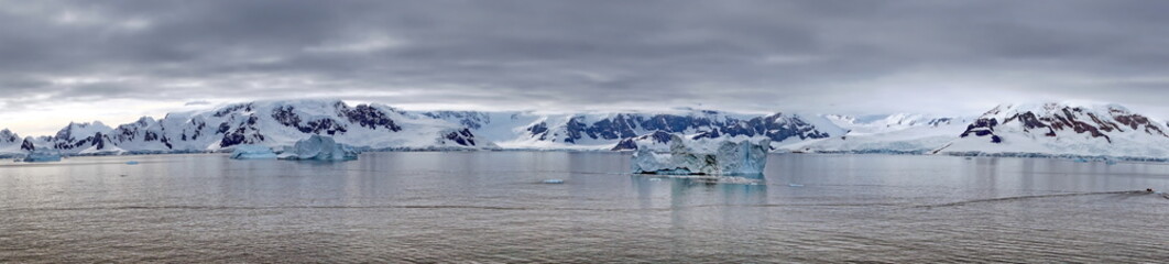 Panorama of icebergs floating in the bay, in front of snow covered moutains at Portal Point in Antarctica