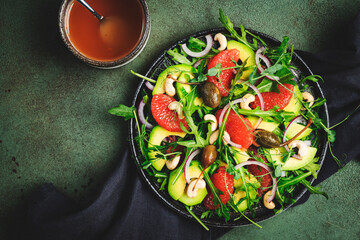 Healthy vegan salad with arugula, avocado, juicy grapefruit, cashews and dressing with olive oil, honey and wine vinegar. Green rustic kitchen table, top view, copy space