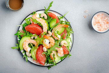 Fresh summer salad with shrimps, avocado, pink grapefruit, arugula and cashews. Gray stone kitchen table background, top view, copy space