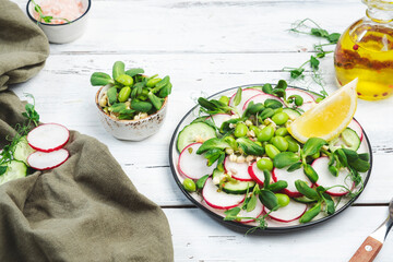 Fresh vegan salad with radish, cucumber, green pea, sunflower and soy sprouts, edamame and flax seeds. Vegetarian healthy diet food. Top view, white kitchen table