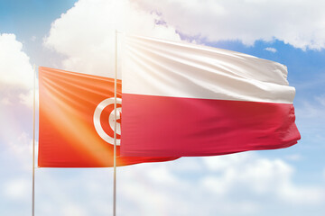 Sunny blue sky and flags of poland and tunisia