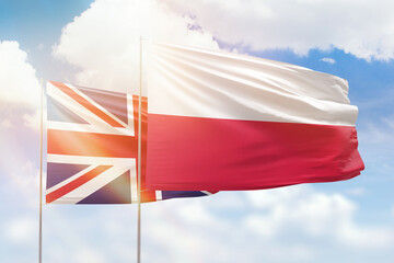 Sunny blue sky and flags of poland and united kingdom