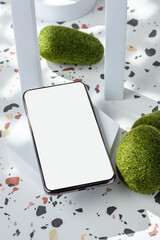 mobile phone on white geometric pedestal on terrazzo background with summer sunlight and moss rock