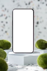 mobile phone on white geometric pedestal on terrazzo background with summer sunlight and moss rock
