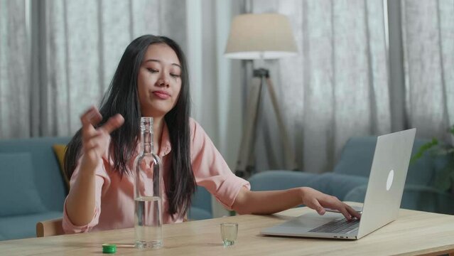 Drunk, Depressed Asian Woman With Smartphone On Table Drinking Vodca From The Bottle At Home
