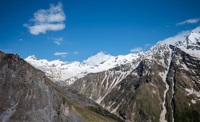 Mountain peaks covered with snow under a blue bright sky with beautiful clouds. Explore the beautiful places of the world. Natural landscape.