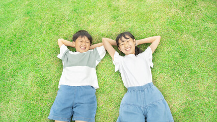 芝生に寝そべる笑顔の小学生の男の子と女の子