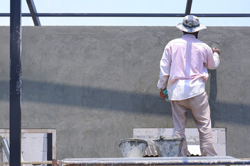 Rear side view of Asian builder worker on scaffolding using wooden trowel polishing cement wall in...
