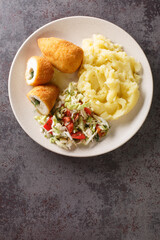 Ukrainian food Kyiv cutlet of chicken fillet with butter and herbs served with mashed potatoes and vegetable salad close-up in a plate on the table. Vertical top view from above
